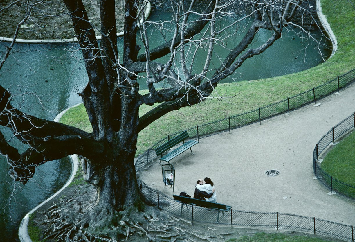 On a cold winter's day in Paris, a couple are in close embrace on a park bench.