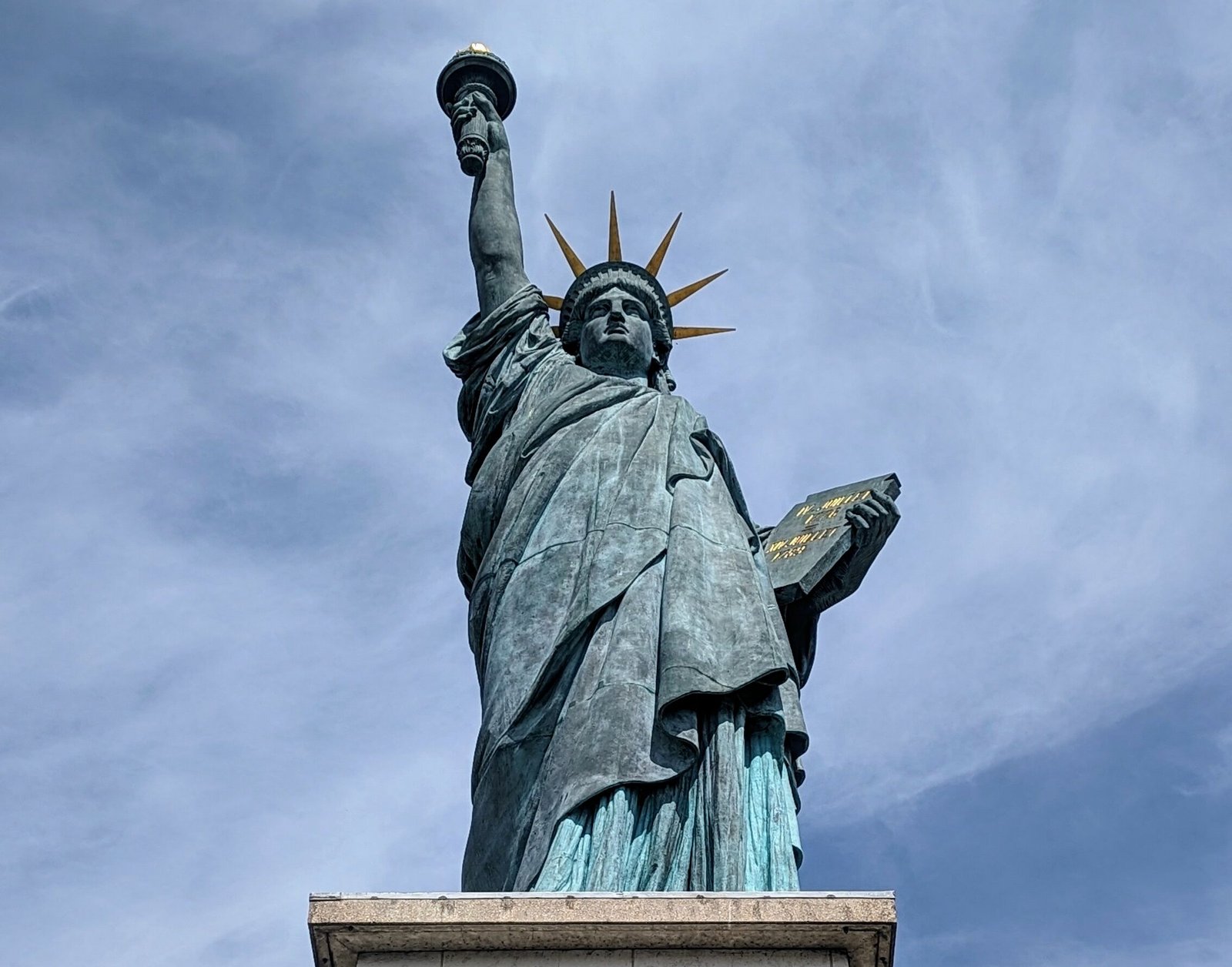 One of the Parisian Statue of Liberty replicas in front of a cloudy blue sky.